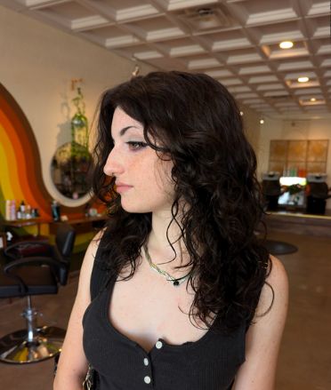 Client with long dark wavy hair in a black tank top, in profile